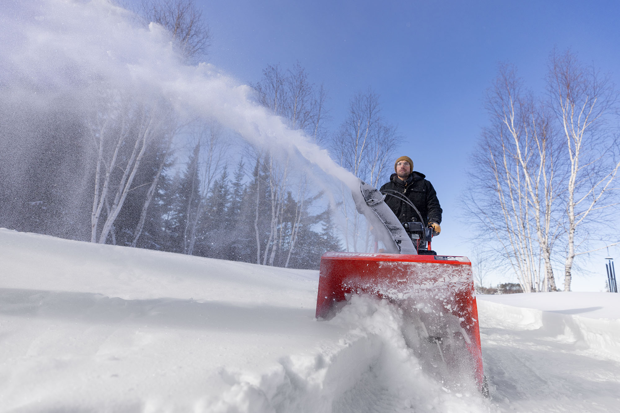 Person walking behind a Troy-Bilt gas powered snow blower clearing their driveway